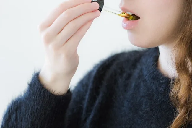 woman, with red hair, dropping cannabis oil under her tongue, wearing a blue sweater
