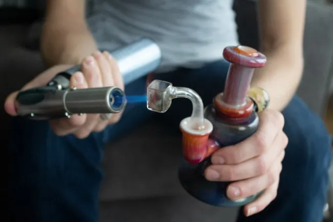 person heating up an orange dab rig with a silver dab torch and blue flame shooting out 