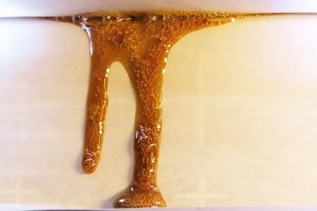 Brownish yellow concentrate liquid oozing from a crack in white parchment paper
