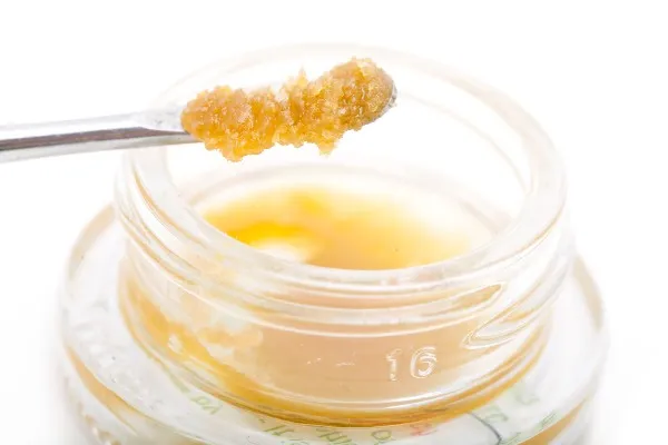 a dab tool with a scoop of orange-yellow cannabis wax over a container of wax