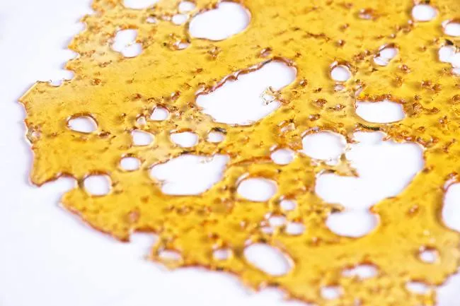 Golden-yellow cannabis shatter that has gaps within the substance like Swiss cheese.