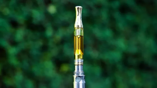 cannabis oil cartridge in a silver battery, against a green nature background
