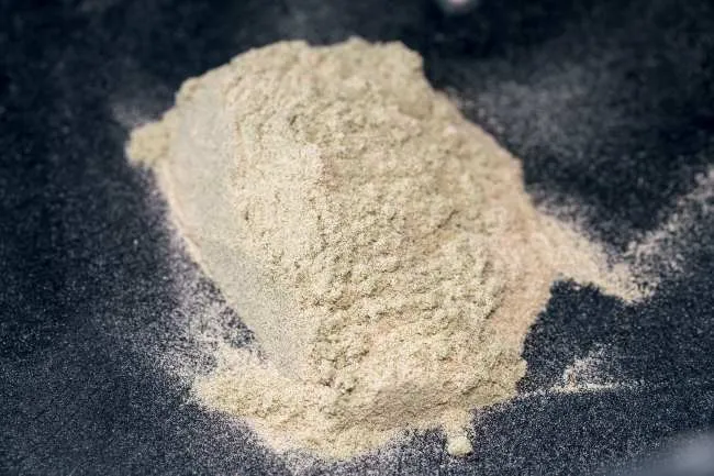 A pile of light yellow white trichome powder that is gathered on top of a black fabric