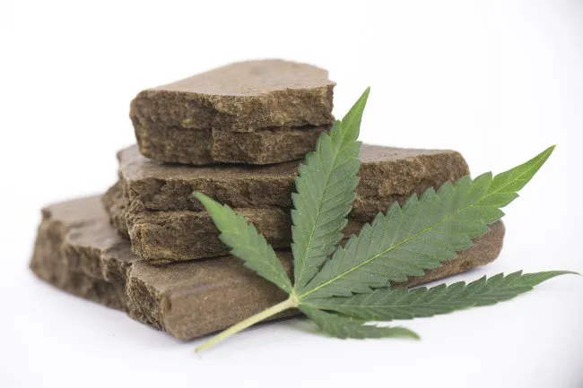 Cannabis hash slabs that are brown and stacked upon each other with a pot leaf lying beside them