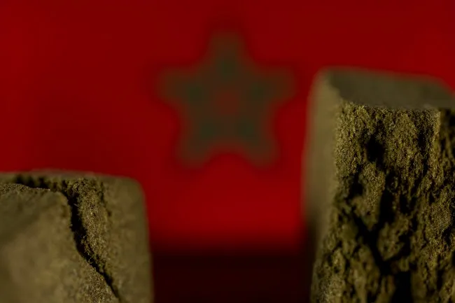 Two piece of brown Moroccan hash with a blurry red and green Moroccan flag in the background