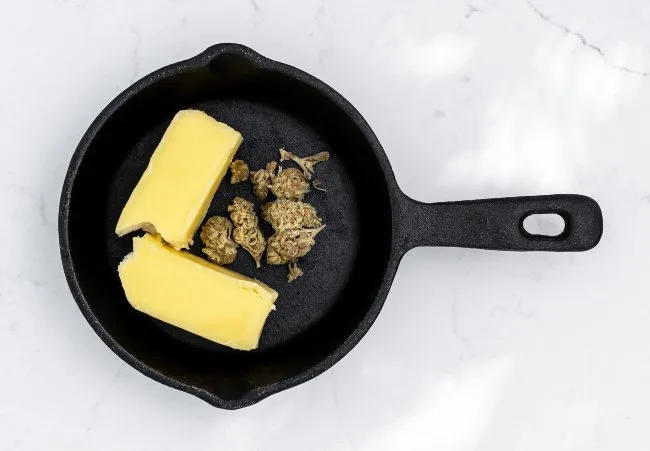 a cast iron pan with butter and cannabis nugs inside